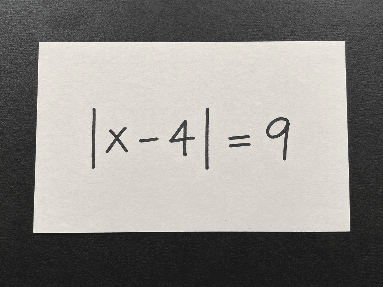 Clear photo of the handwritten absolute-value equation absolute value of x minus 4 equals 9